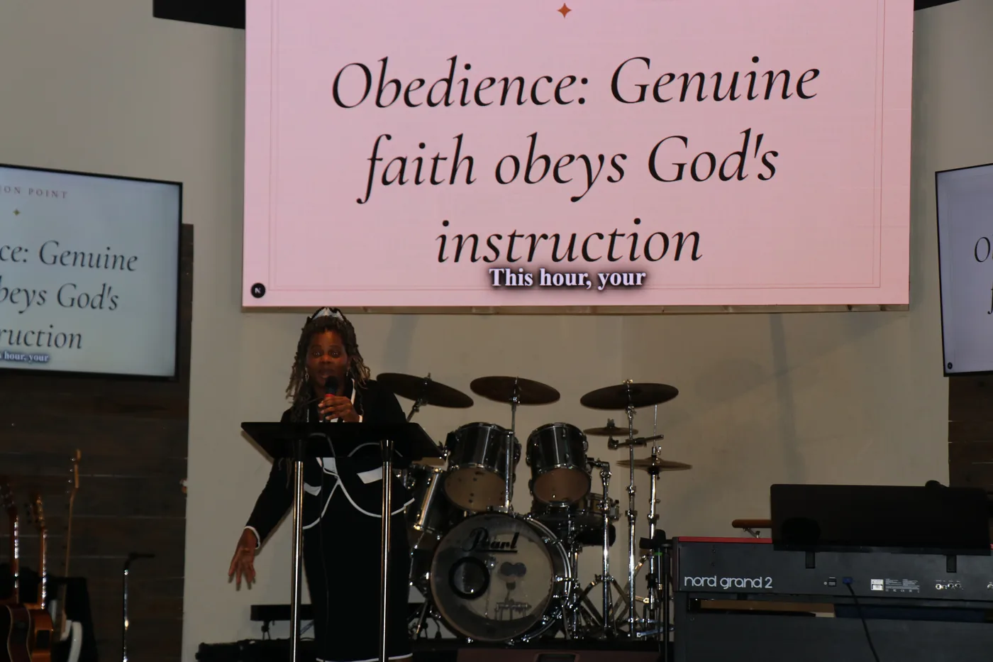 A speaker mid-sentence at a podium, with a sermon point already on the screen behind her and a live caption of her words underneath it.