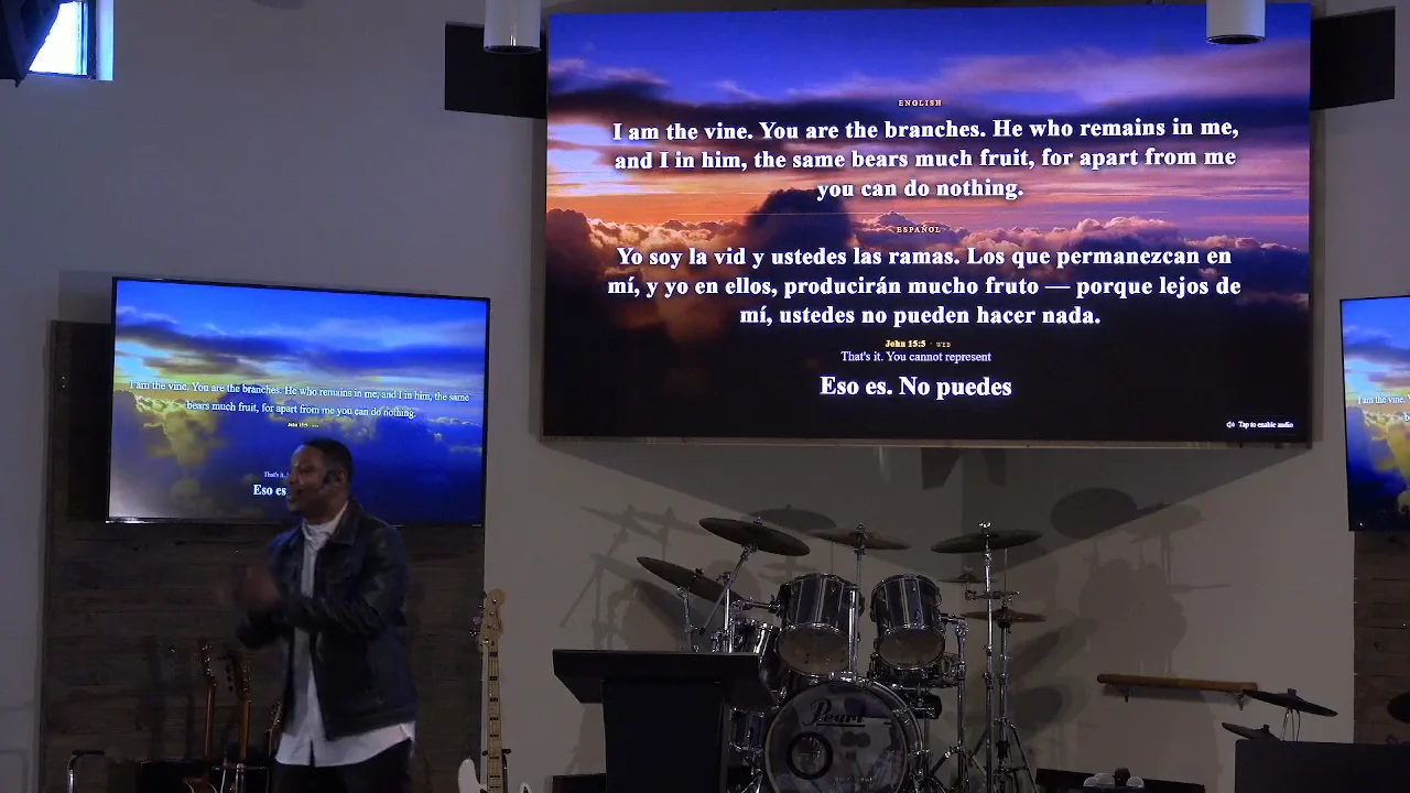 A church screen showing John 15 verse 5 in English and again in Spanish, with a live caption of the speaker's words beneath it.